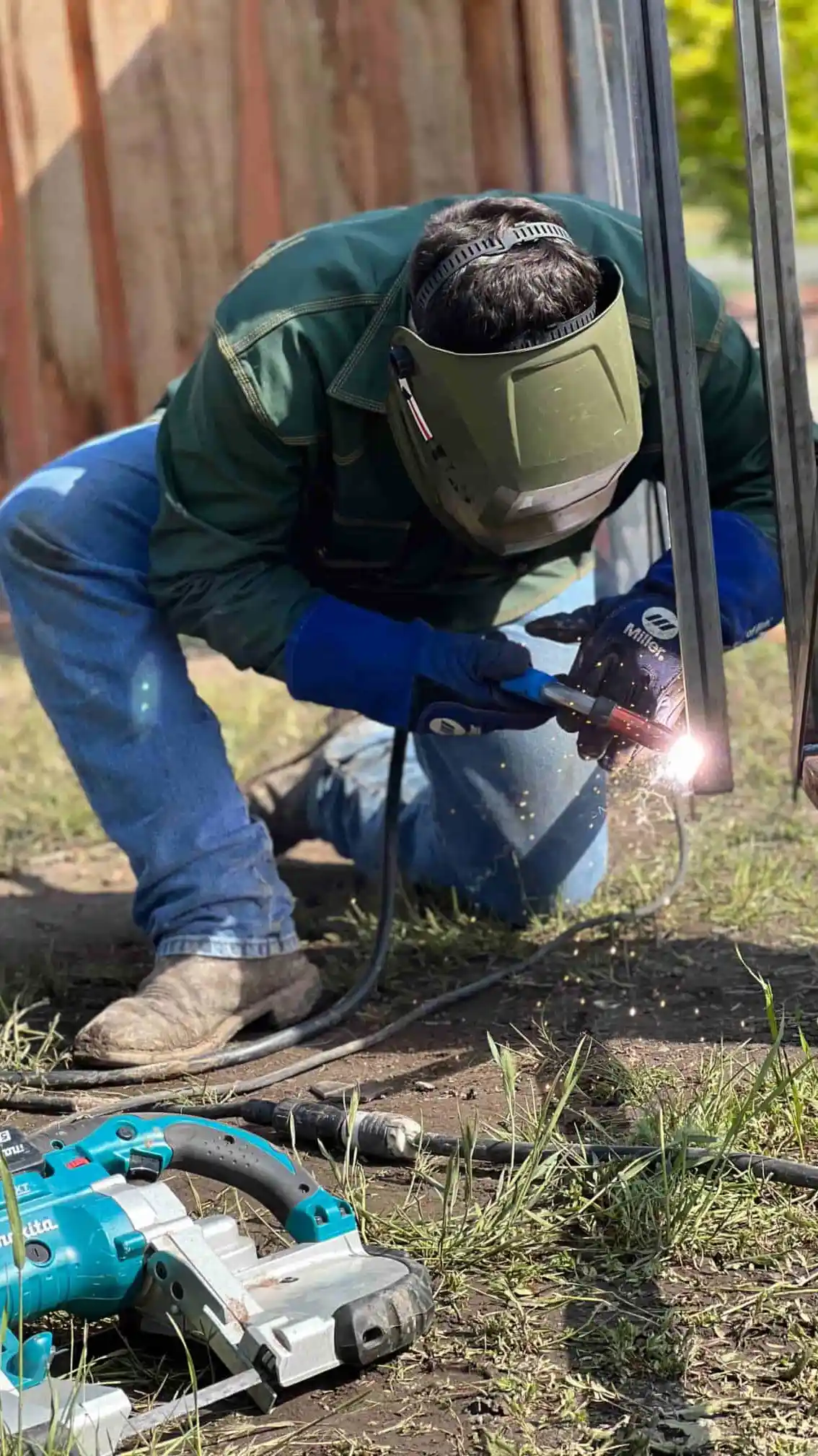 person crouching welding a metal frame on fence