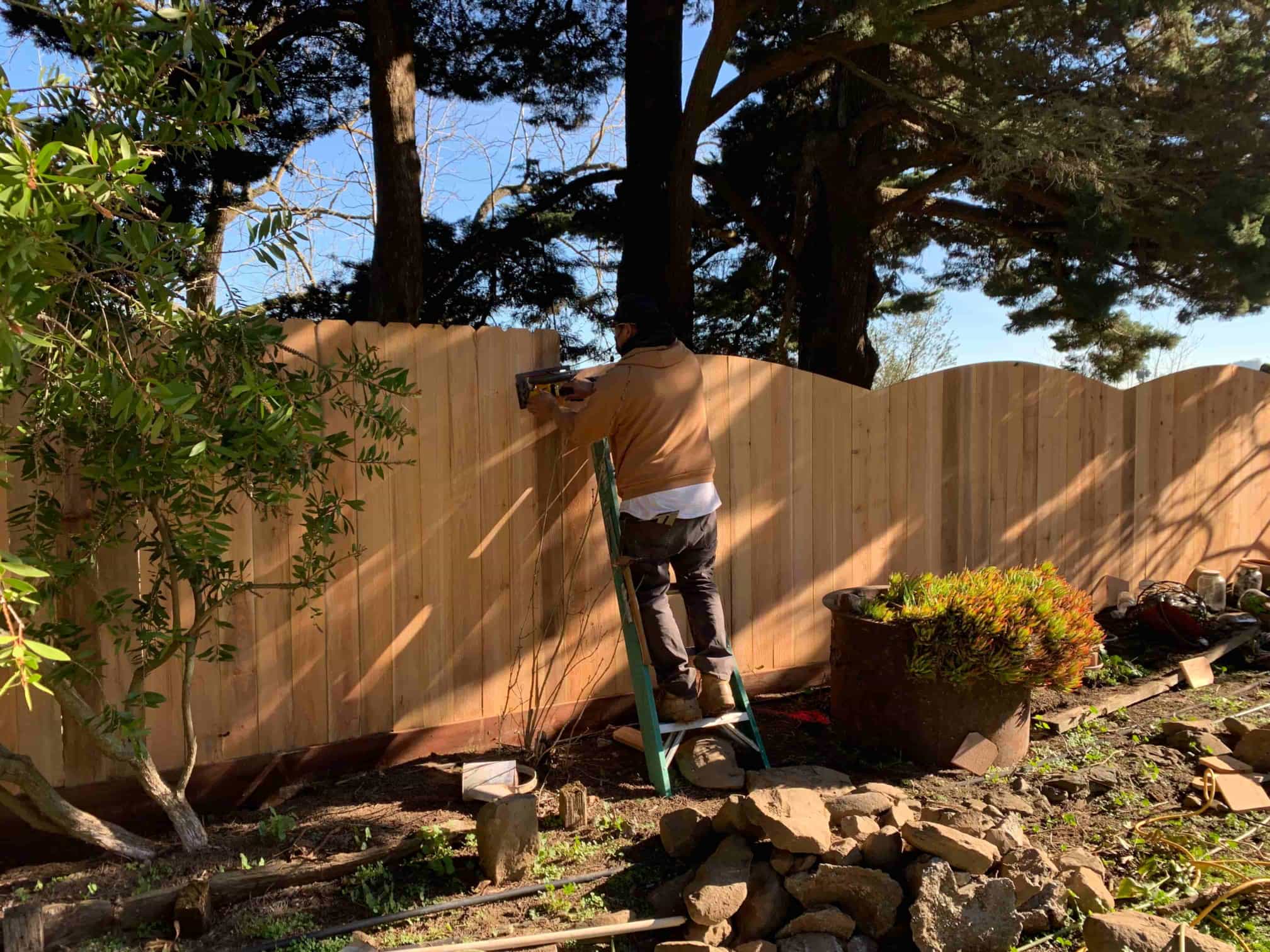 guy on ladder using a nail gun on fence