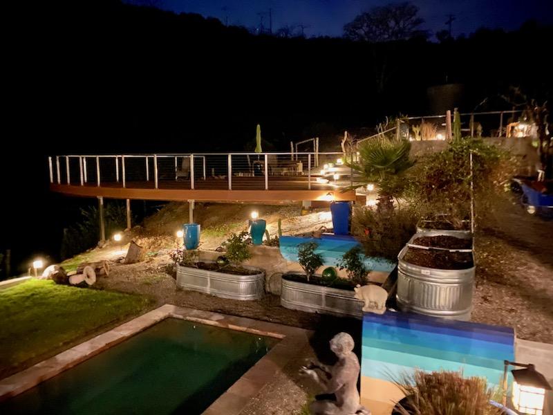 deck over a ledge with a metal gate at night with lights on in garden