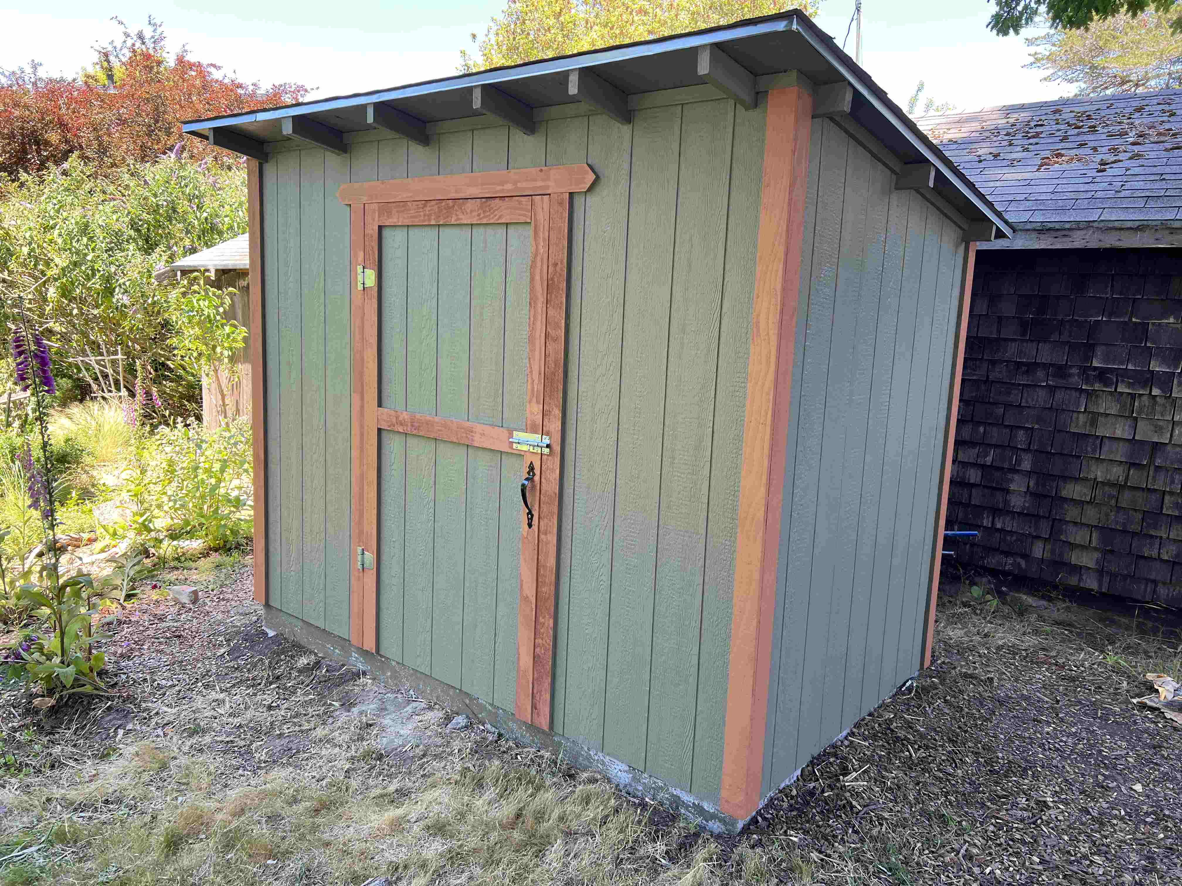 green tool shed with foliage in the background